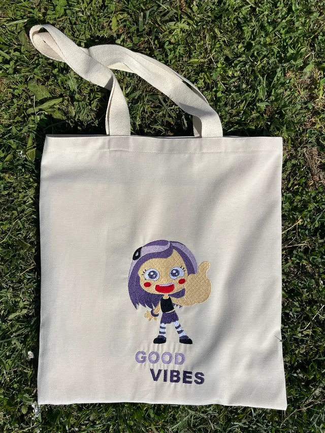 Makine nakışıyla çizgi film karakteri bir kız ve “Good Vibes” yazısı işlenmiş bez çanta